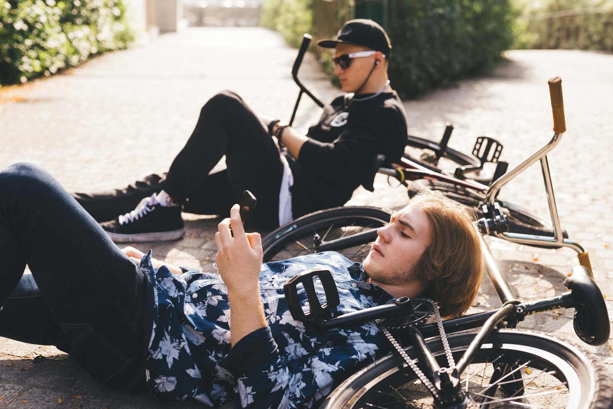 Two young sportive men teenagers relaxing phubbing using smartphone